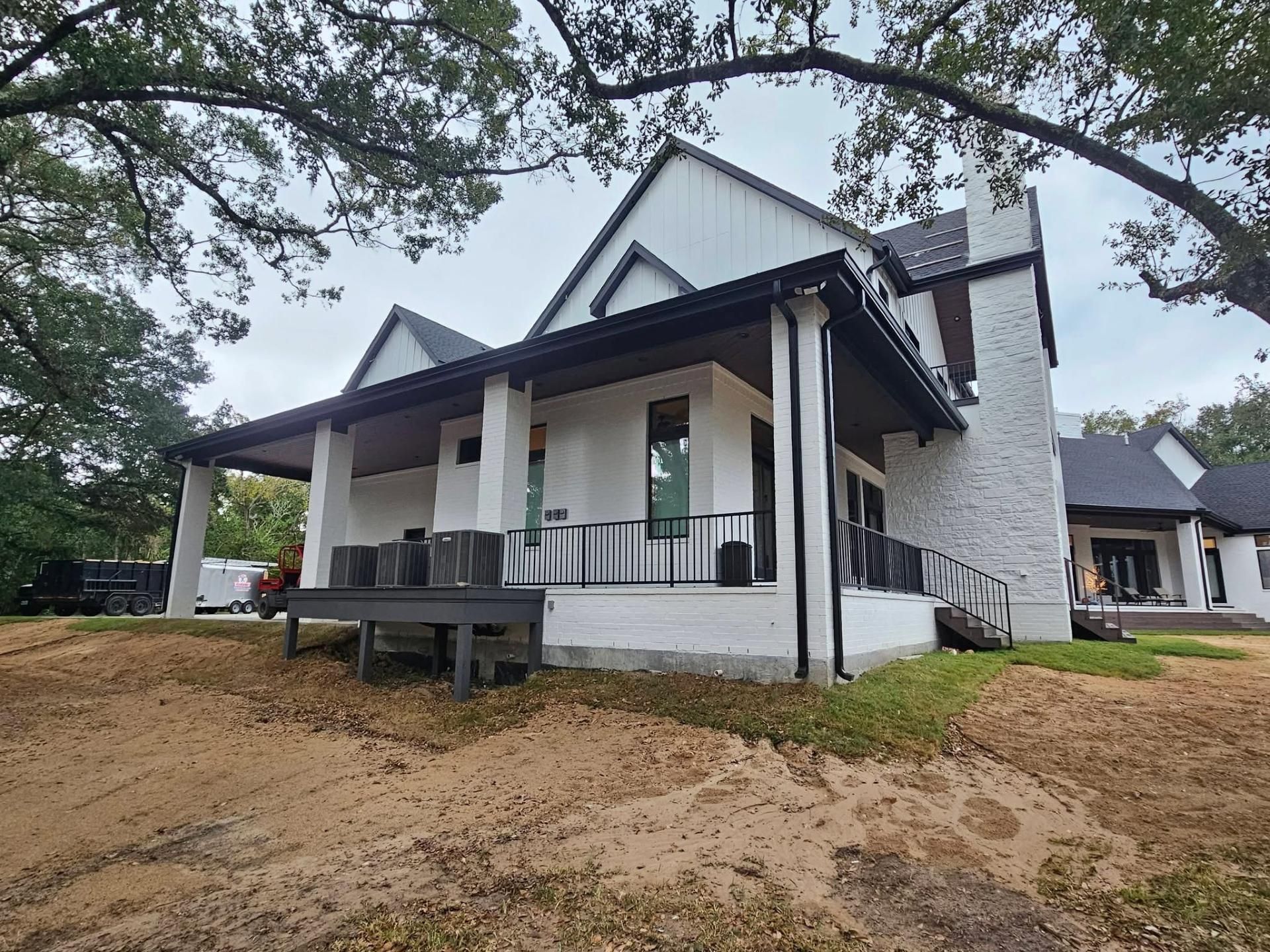 White house with black trim, porch, and brick chimney on a cloudy day.
