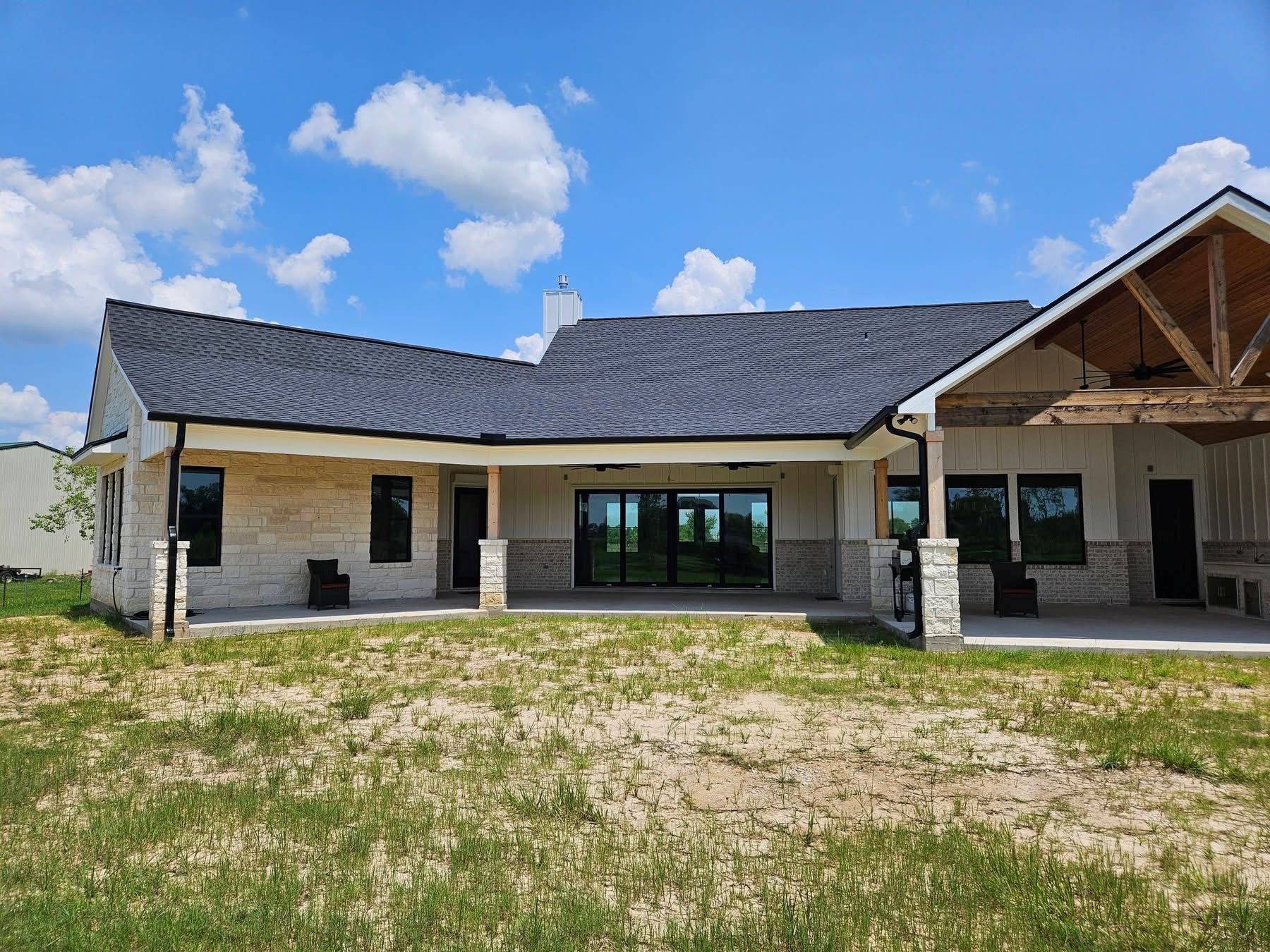 Back view of a light-colored stone house with a dark gray roof under a blue sky.