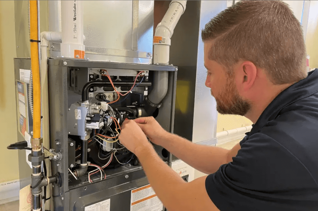 HVAC technician repairing furnace wiring. Indoors, focused, with tools.
