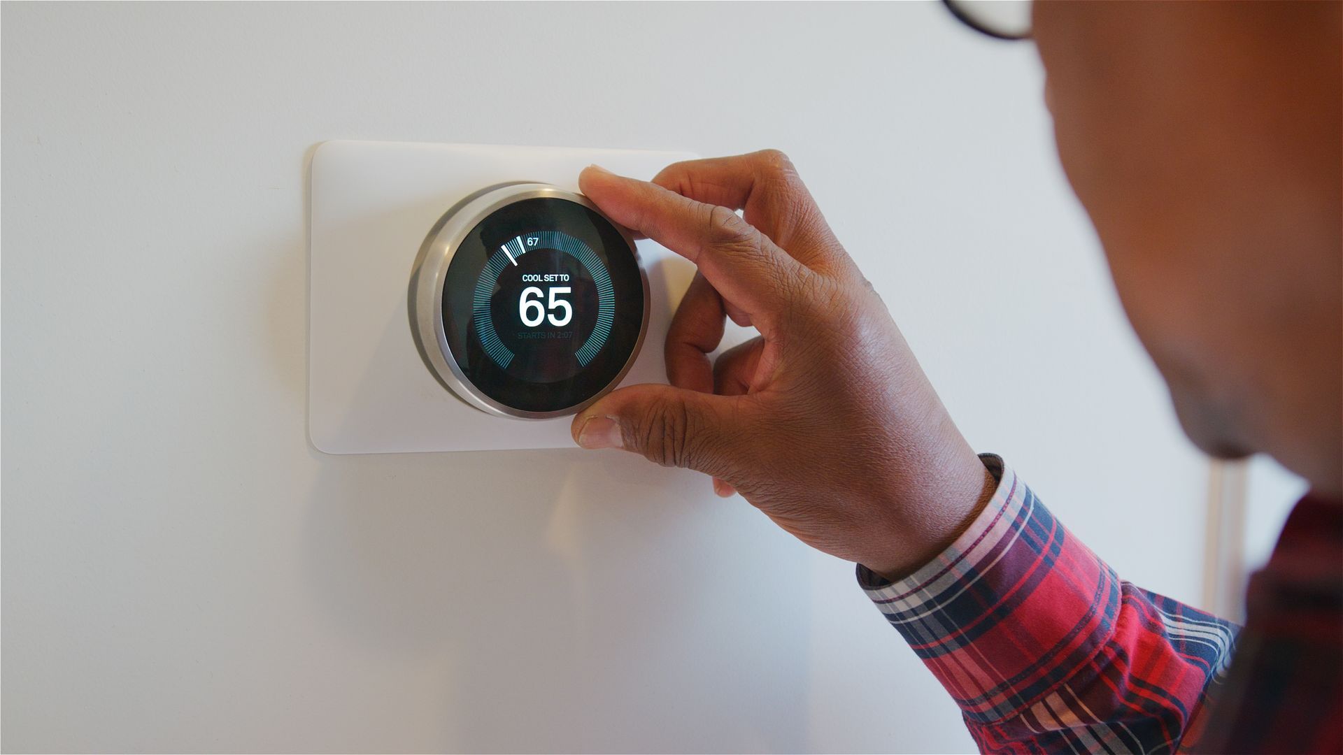 Person adjusting a smart thermostat set to 65 degrees.