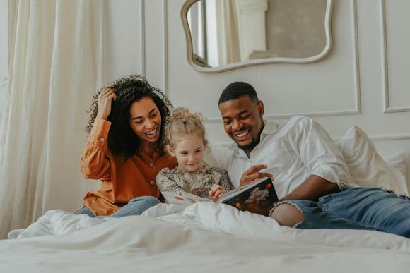Family sitting on a bed, smiling and looking at a tablet in a bright bedroom
