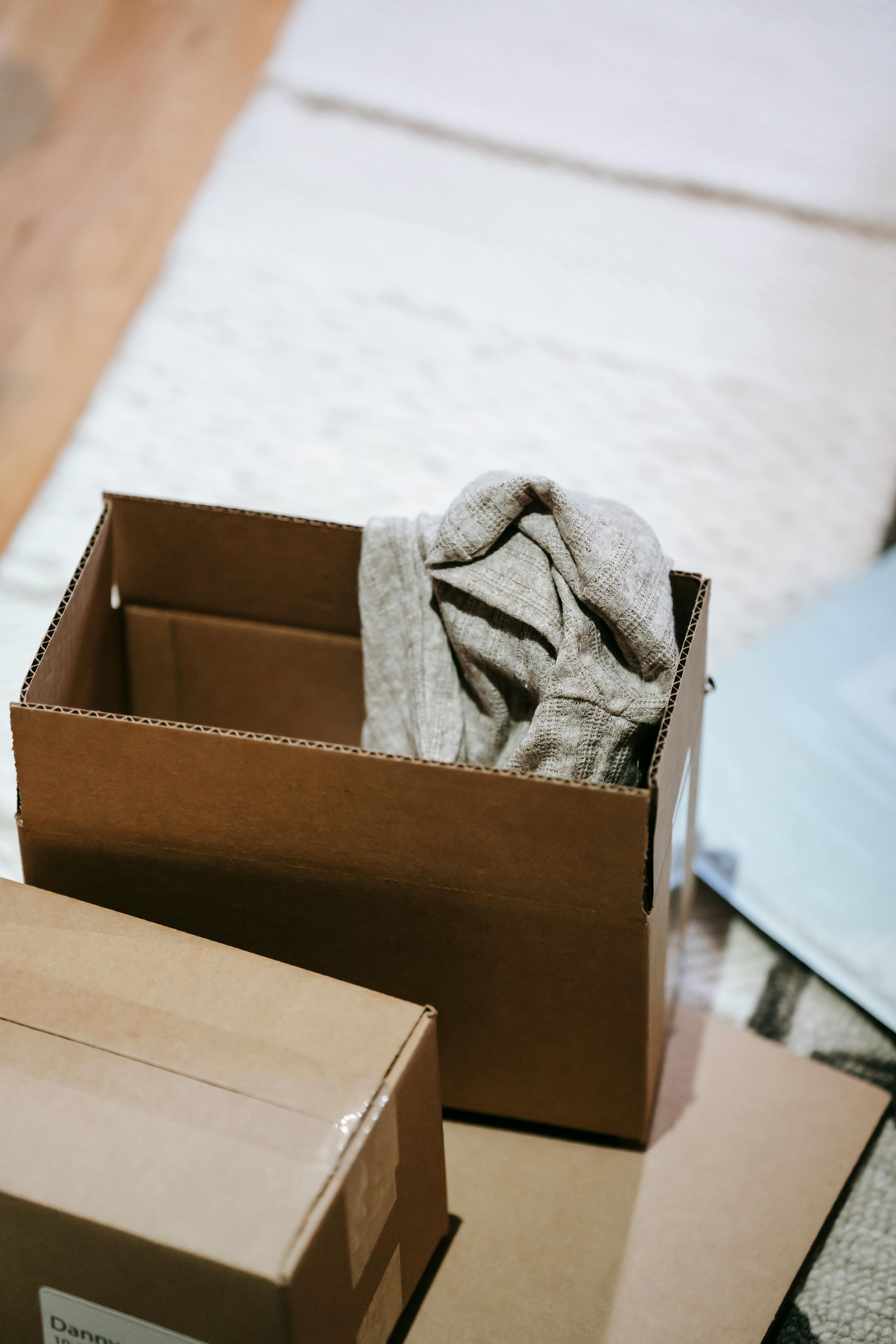 Cardboard box with a sweater, near other boxes and a rug.