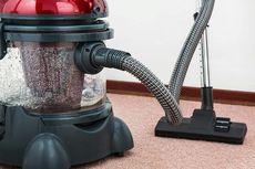 Red and black wet-dry vacuum cleaner with a clear water tank, hose, and carpet brush head on a carpet.