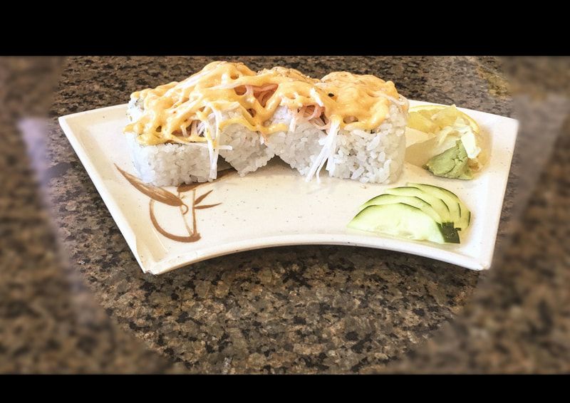 Sushi rolls topped with shredded cheese on a white plate, with avocado slices on the side.