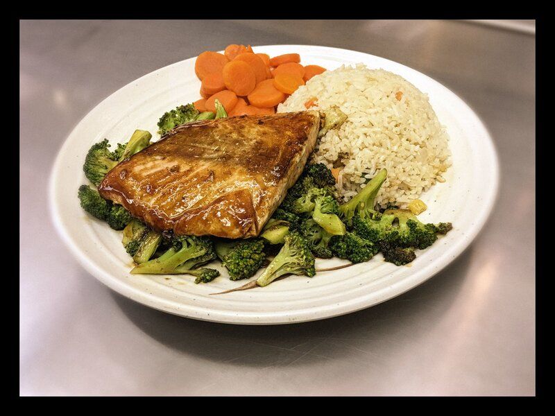 Grilled salmon with rice, broccoli, and carrots on a white plate