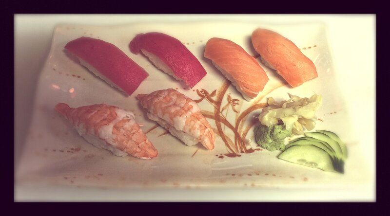 Assorted sushi nigiri on a white platter with wasabi and sliced cucumber garnish