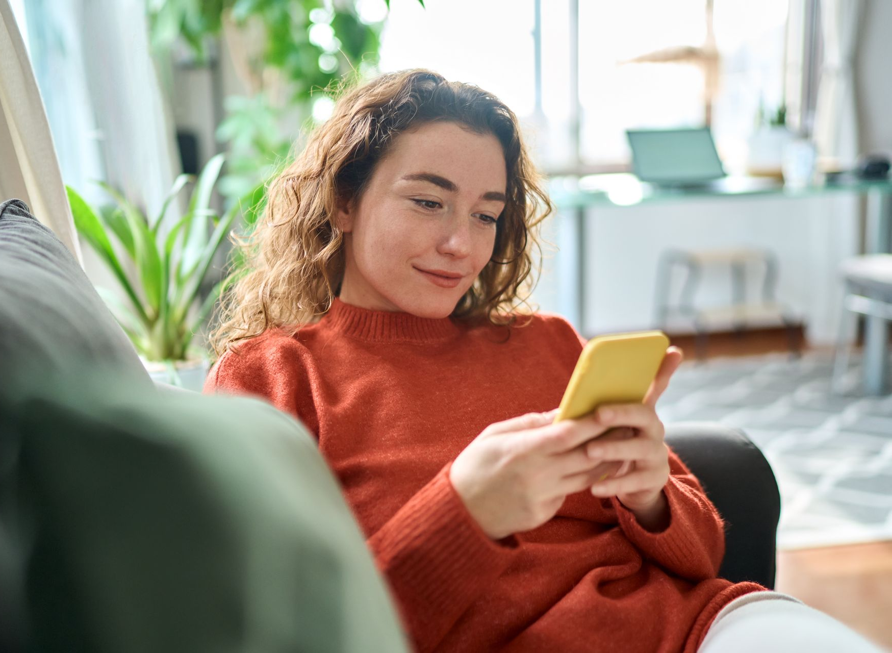 Woman with curly hair using a yellow phone, sitting on a sofa in a living room.