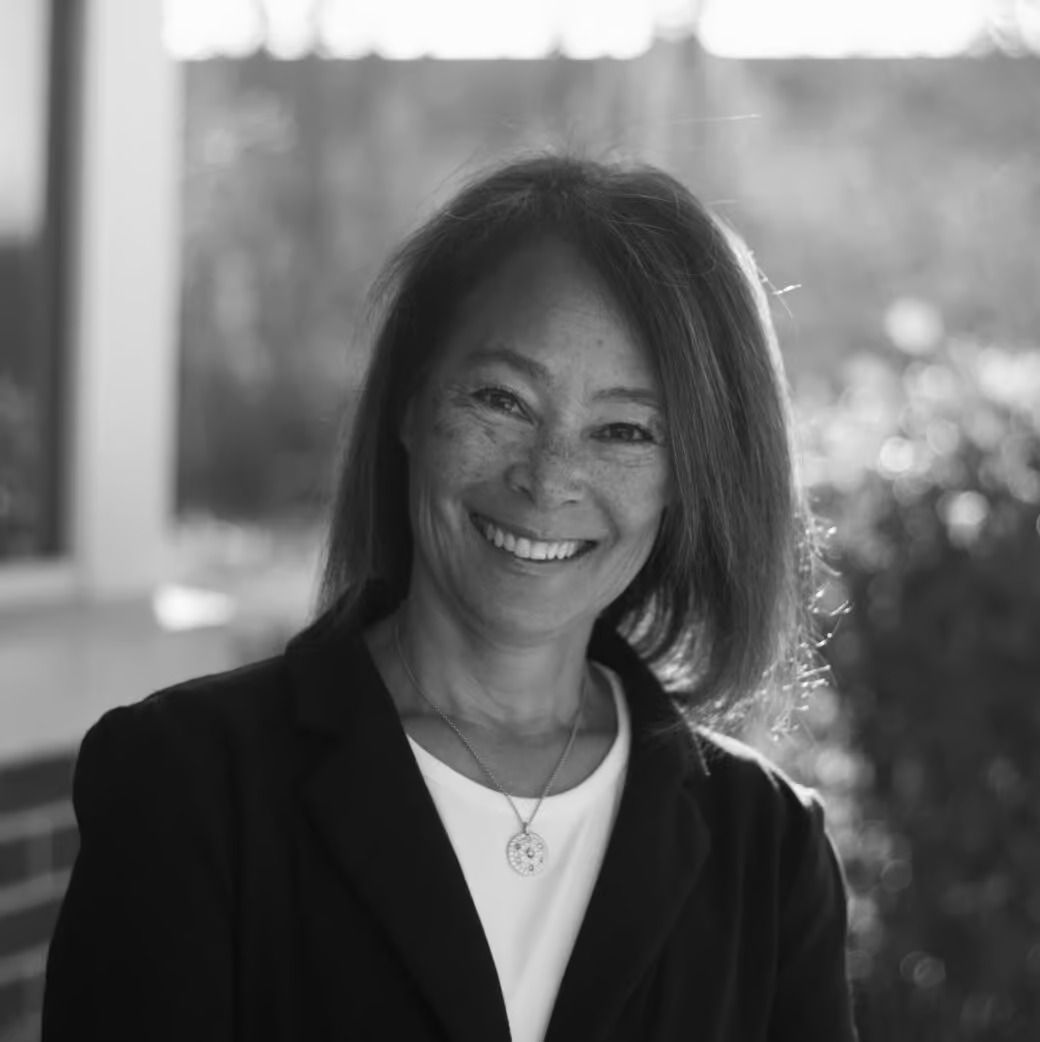 Smiling woman with brown hair in a dark blazer. Outdoor setting.