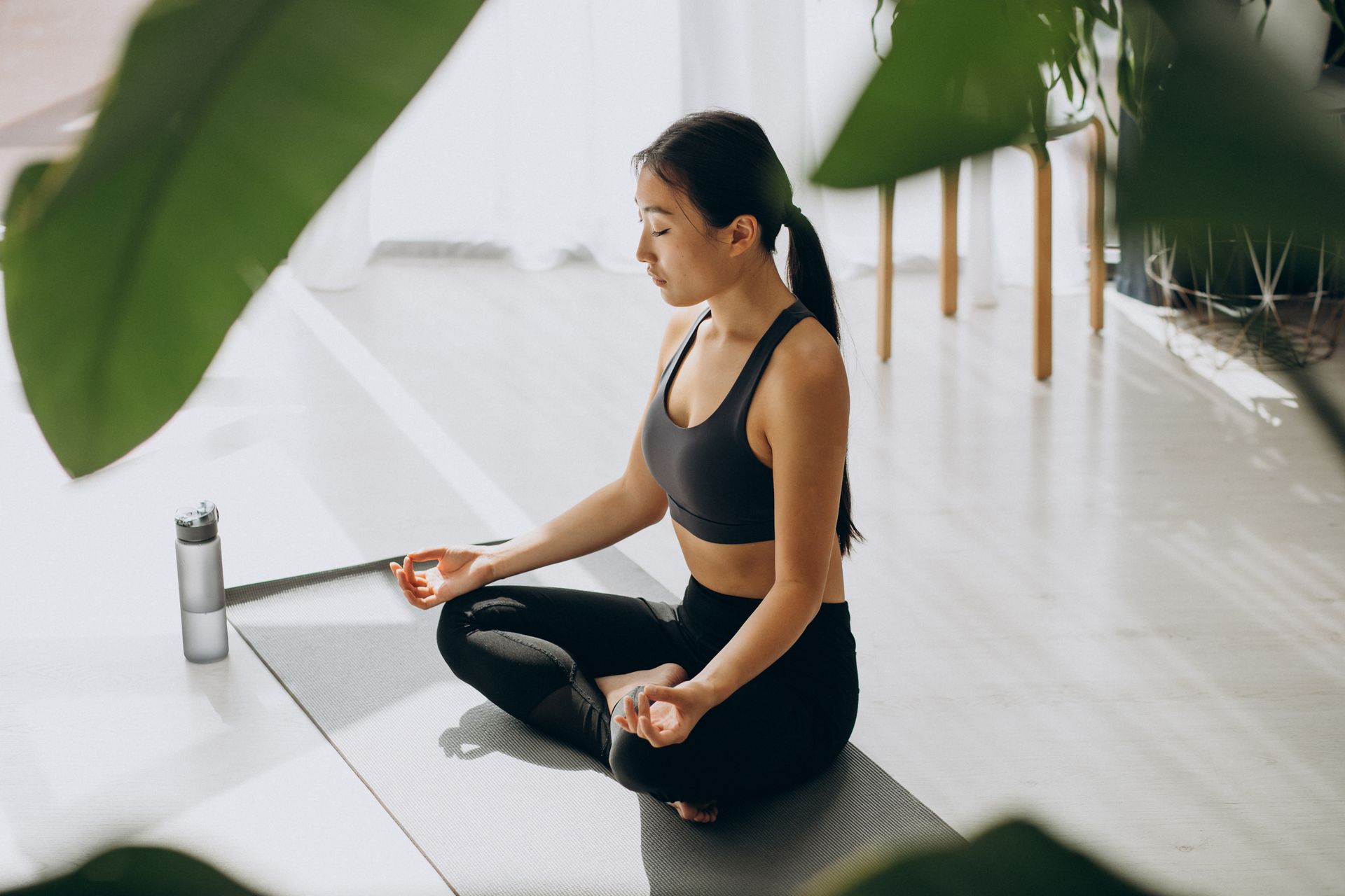 Woman in athletic wear meditating on a yoga mat with eyes closed, indoors.