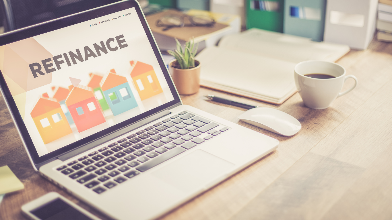 A laptop computer is sitting on a wooden desk with the word refinance on the screen.