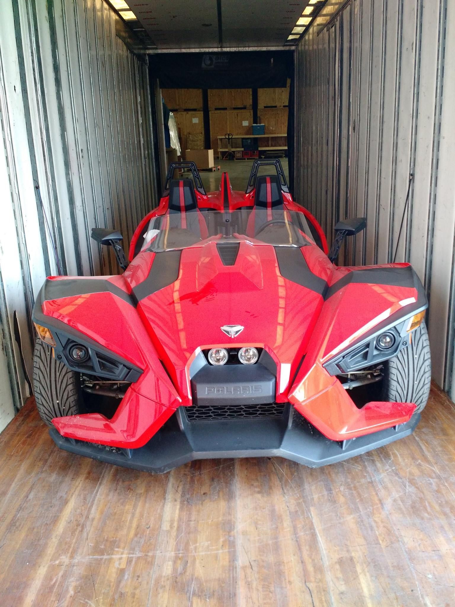 Red Polaris Slingshot three-wheeled vehicle inside a cargo container, ready for transport.
