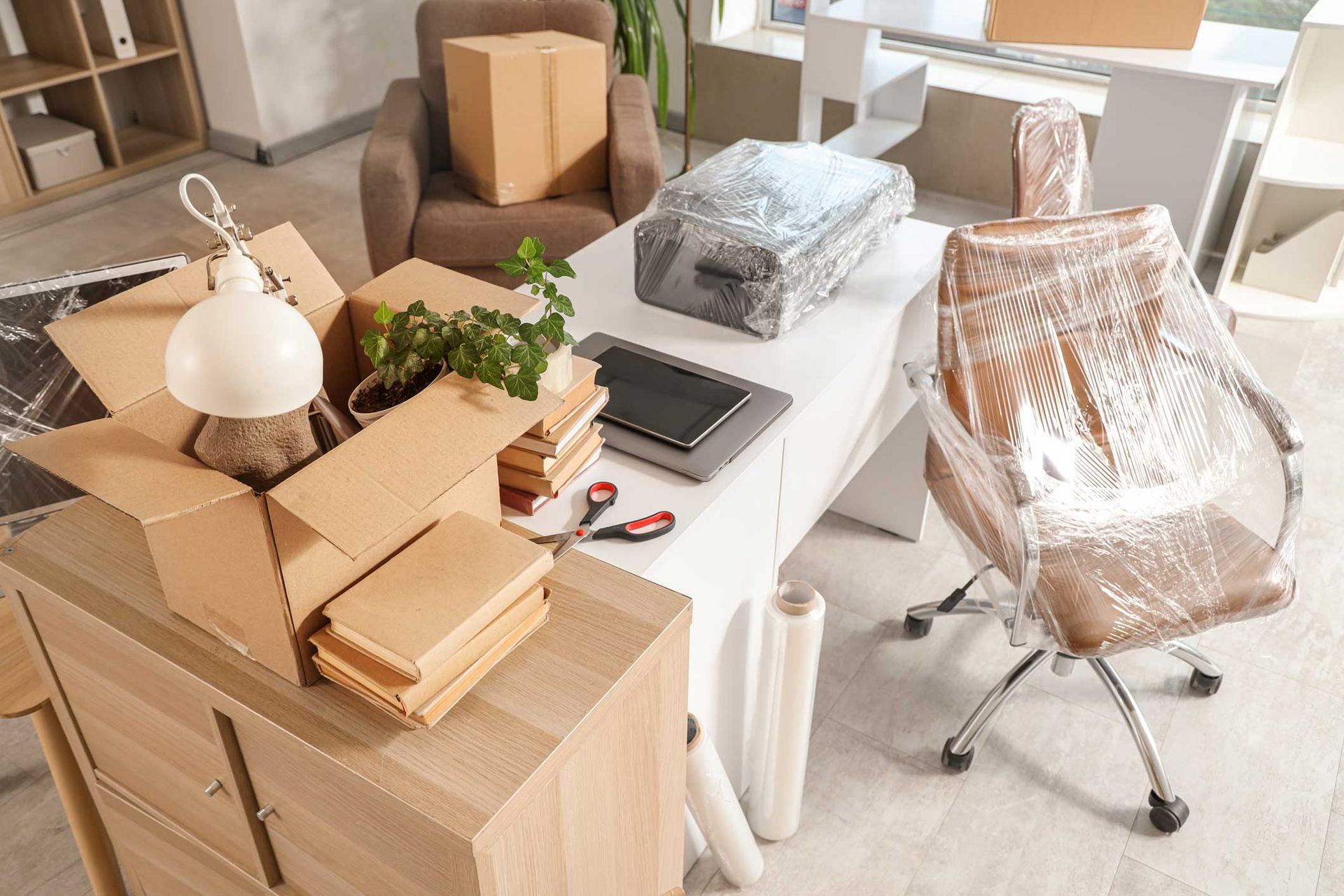 Office interior with desk, moving boxes, and stretch-wrapped chairs
