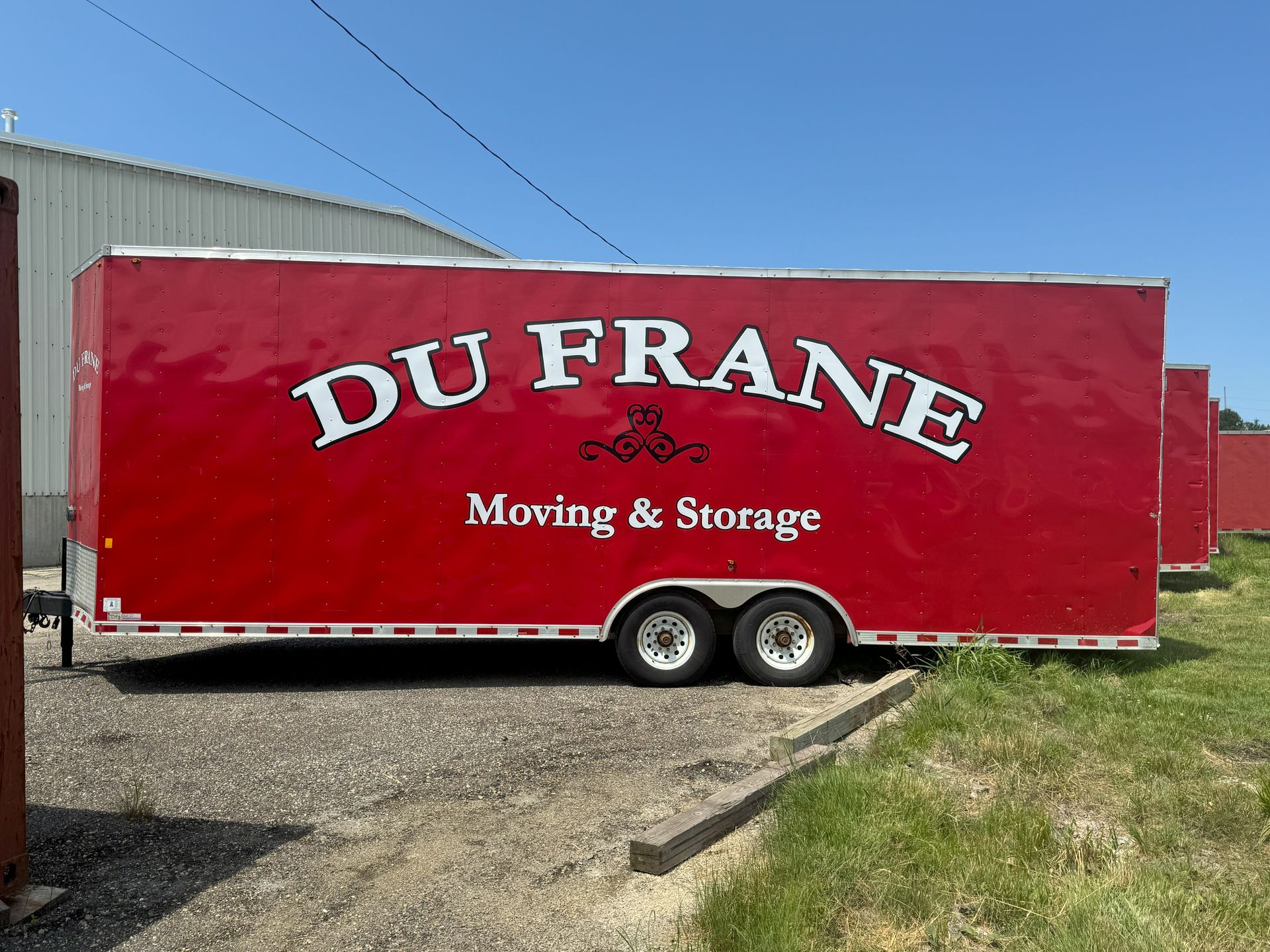 Red Du Frane Moving & Storage trailer on gravel with a green grassy area and a light blue sky.