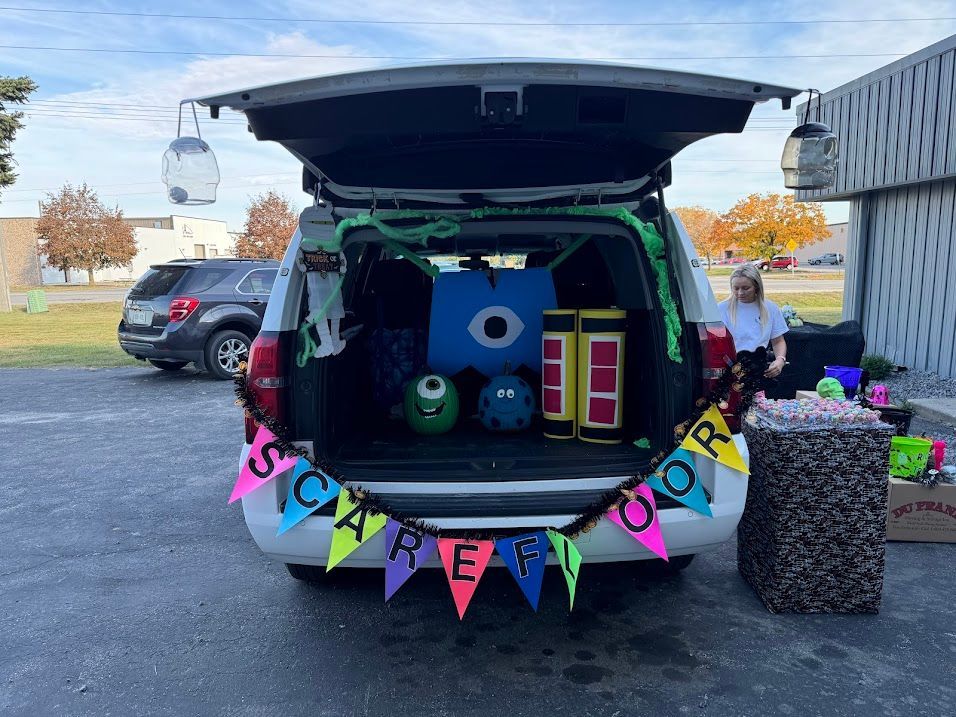 Trunk-or-treat car decorated with colorful “spooky” banner, blue monster, and bright Halloween props.