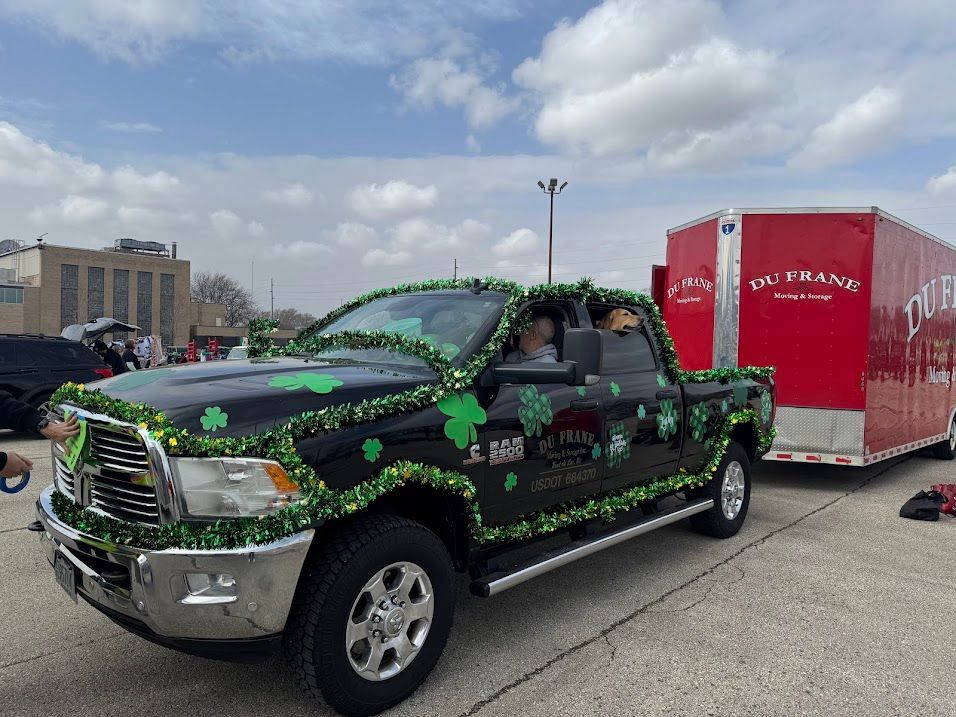 Black pickup with green vine graphics parked beside a red trailer in a parking lot under a cloudy sky