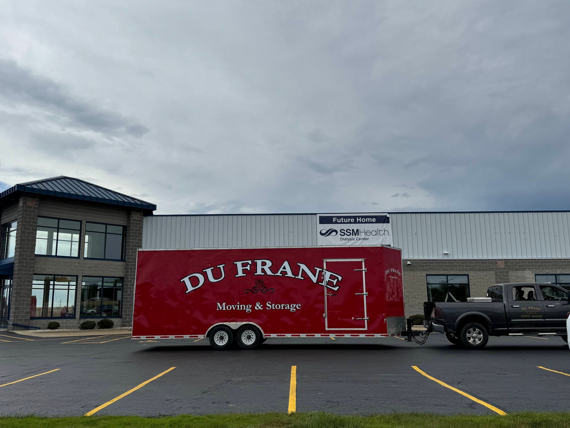 Red DU FRANE trailer parked outside a storefront on an overcast day.