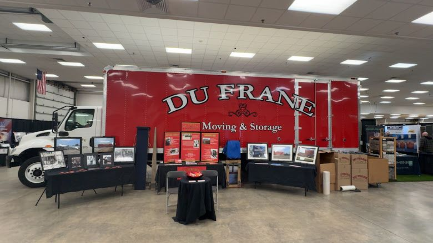 Trade show booth with a large red DuFrane Moving & Storage banner, tables, and display monitors.