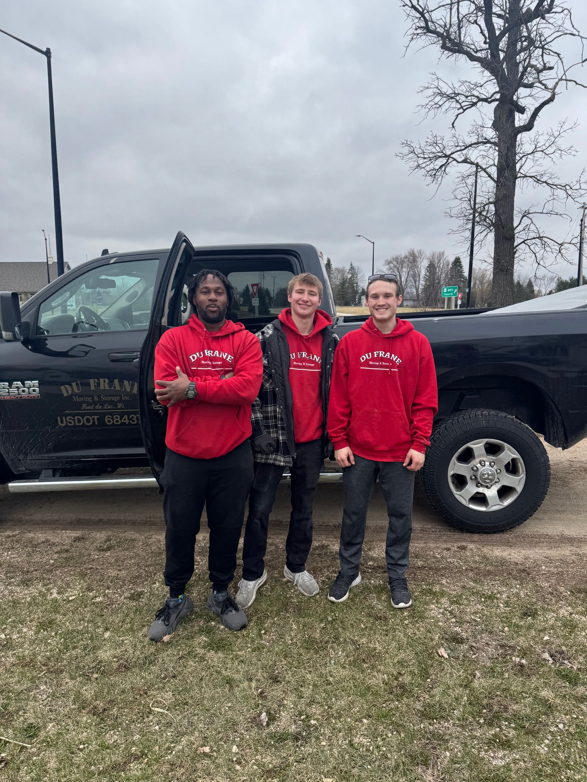 Three people in red hoodies stand by a black pickup truck on a cloudy day.