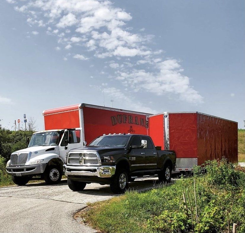 Two trucks, one white, one black, pulling a large red trailer outdoors on a sunny day.
