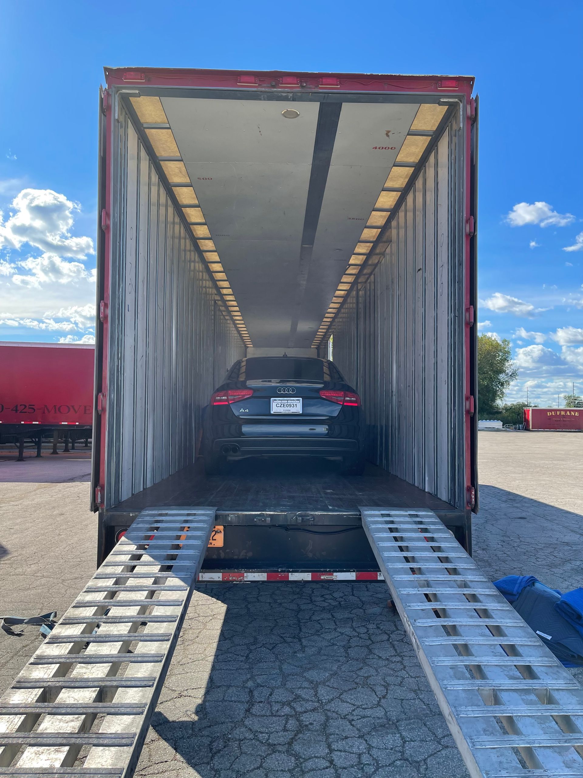 A black car inside a car hauler truck, seen from the open ramp.