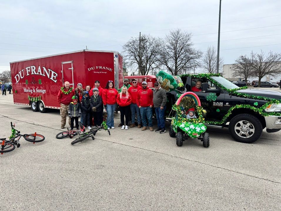 Group of people posing beside a red Budweiser truck and decorated black pickup with holiday wreaths, bicycles in front