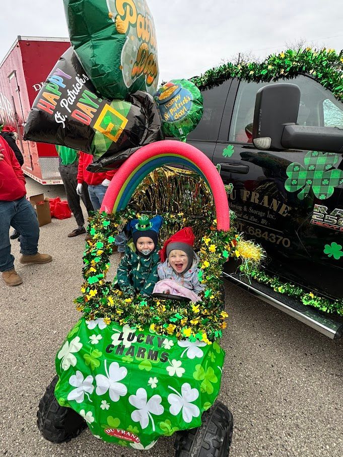 Decorated green parade car with two children, rainbow arch, clovers, and balloons on a street float