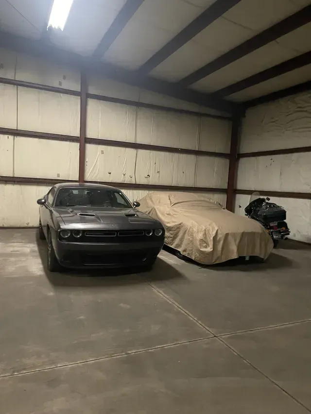 Dark gray Dodge Challenger in a warehouse next to a covered vehicle and motorcycle.