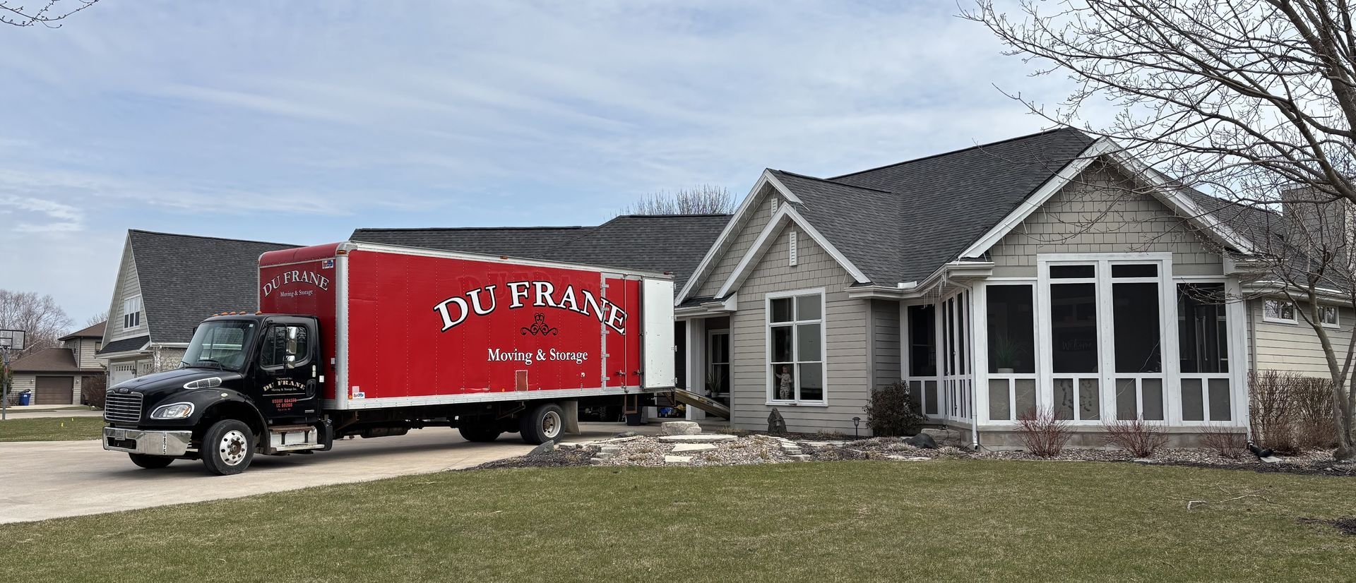 Red moving truck parked in front of a gray house.