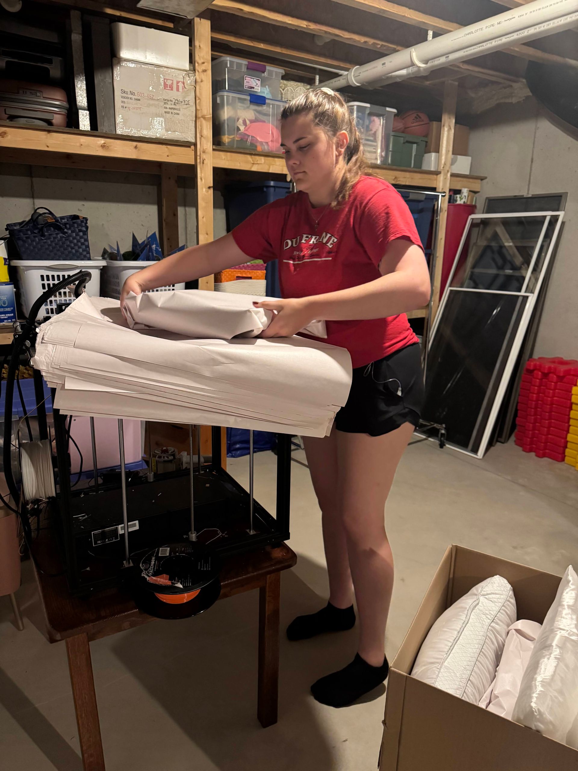 Person folding white linens on a table in a basement storage area