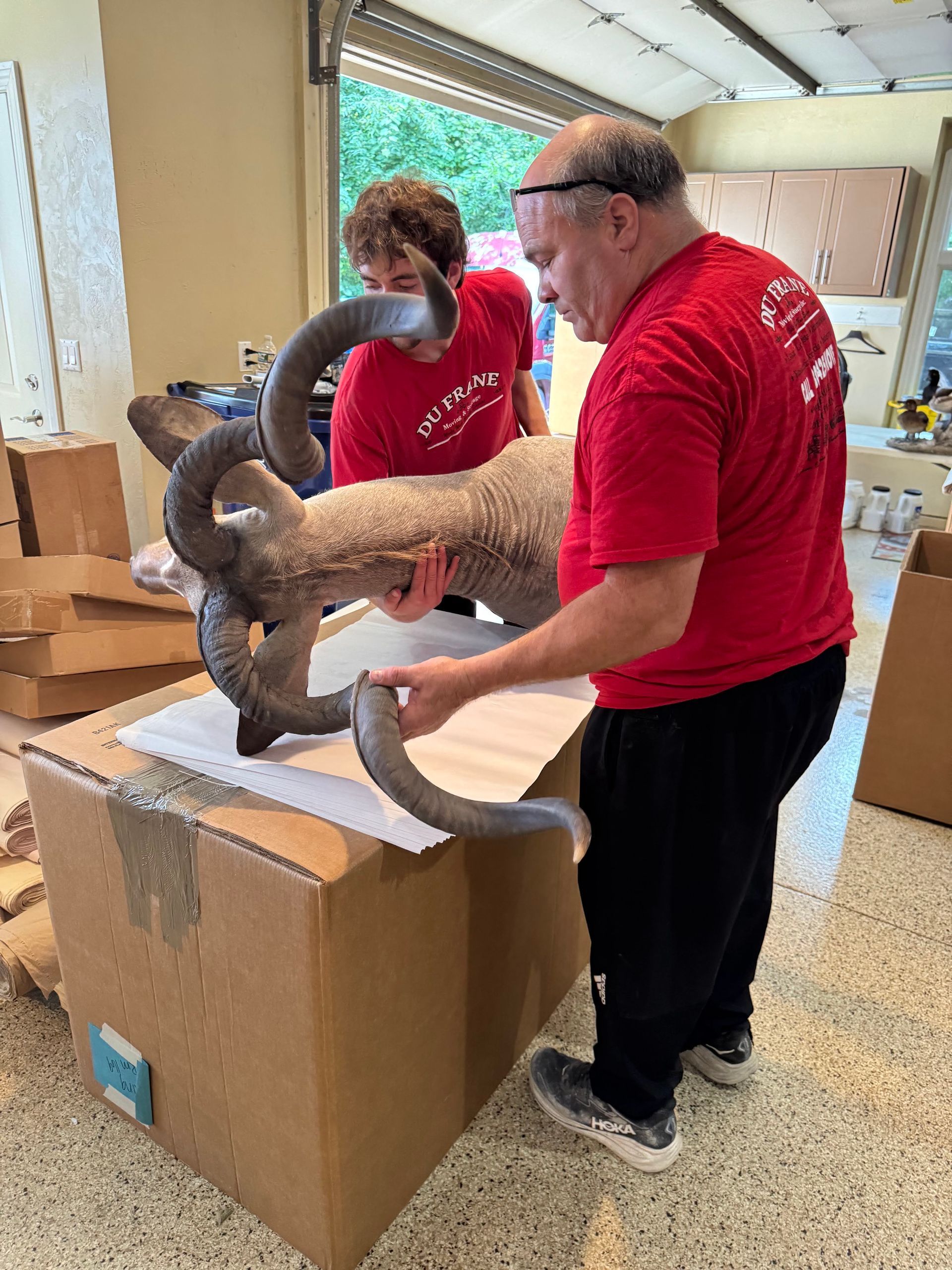 Two people in red shirts handling a large horned animal sculpture in a workshop