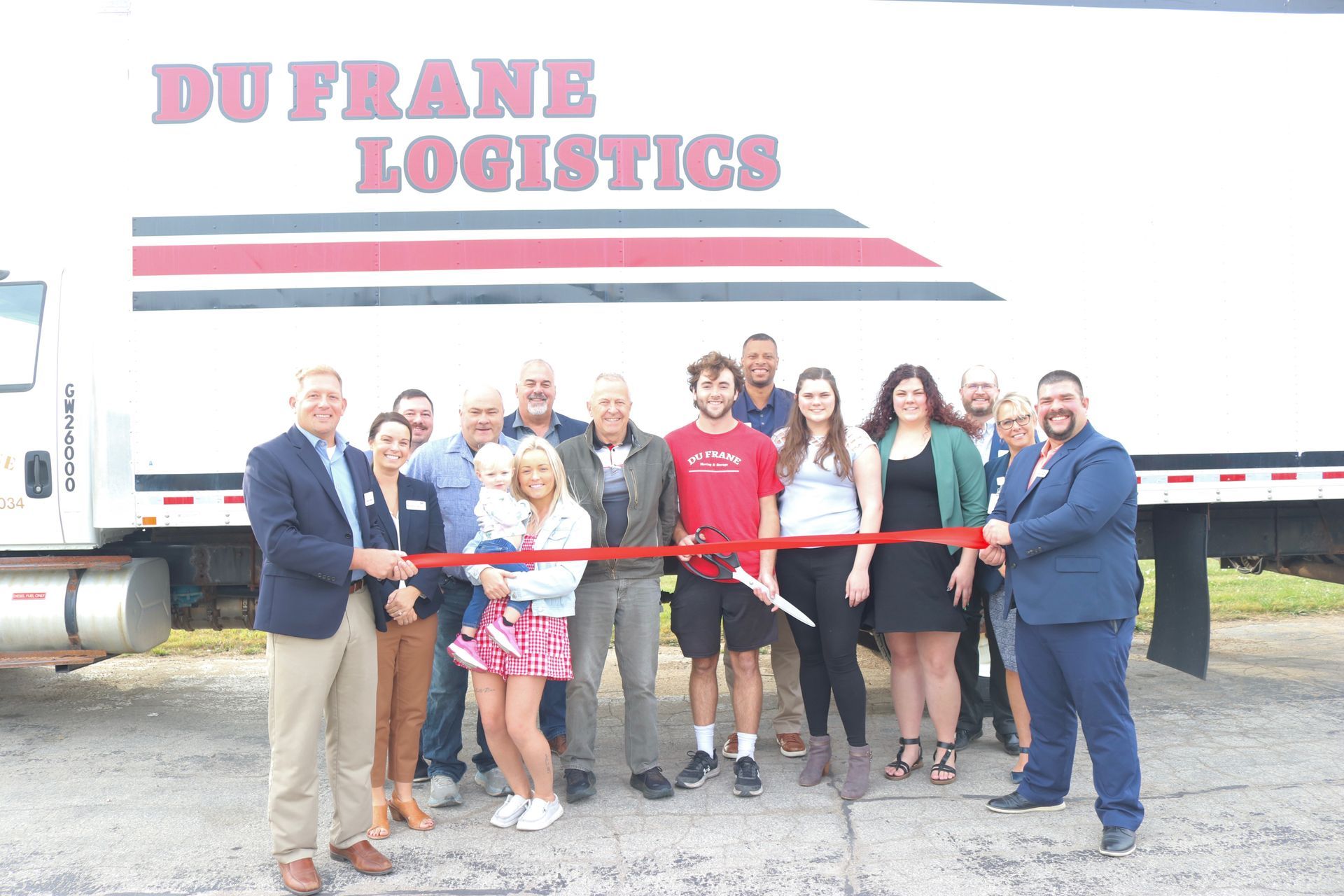 People cutting a ribbon in front of a Du Frane Logistics truck at an outdoor event.