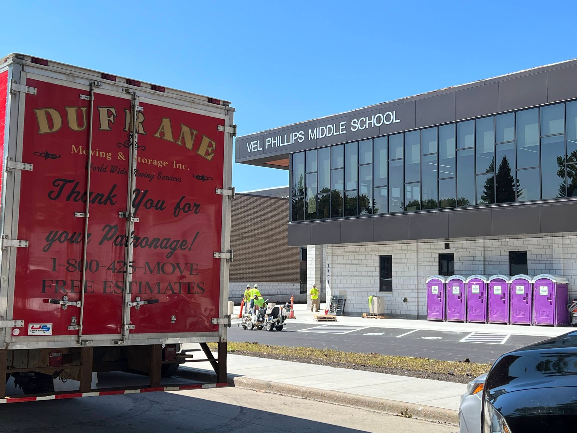 Red moving truck parked near the Vel Phillips & Dale School building with purple portable toilets.