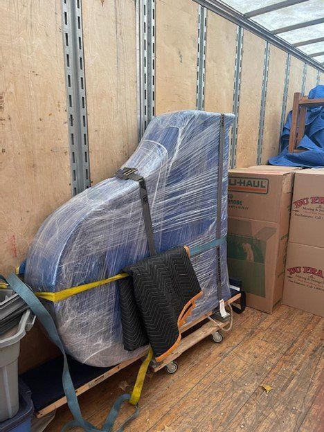 A blue chair wrapped in plastic and secured with straps inside a U-Haul truck.