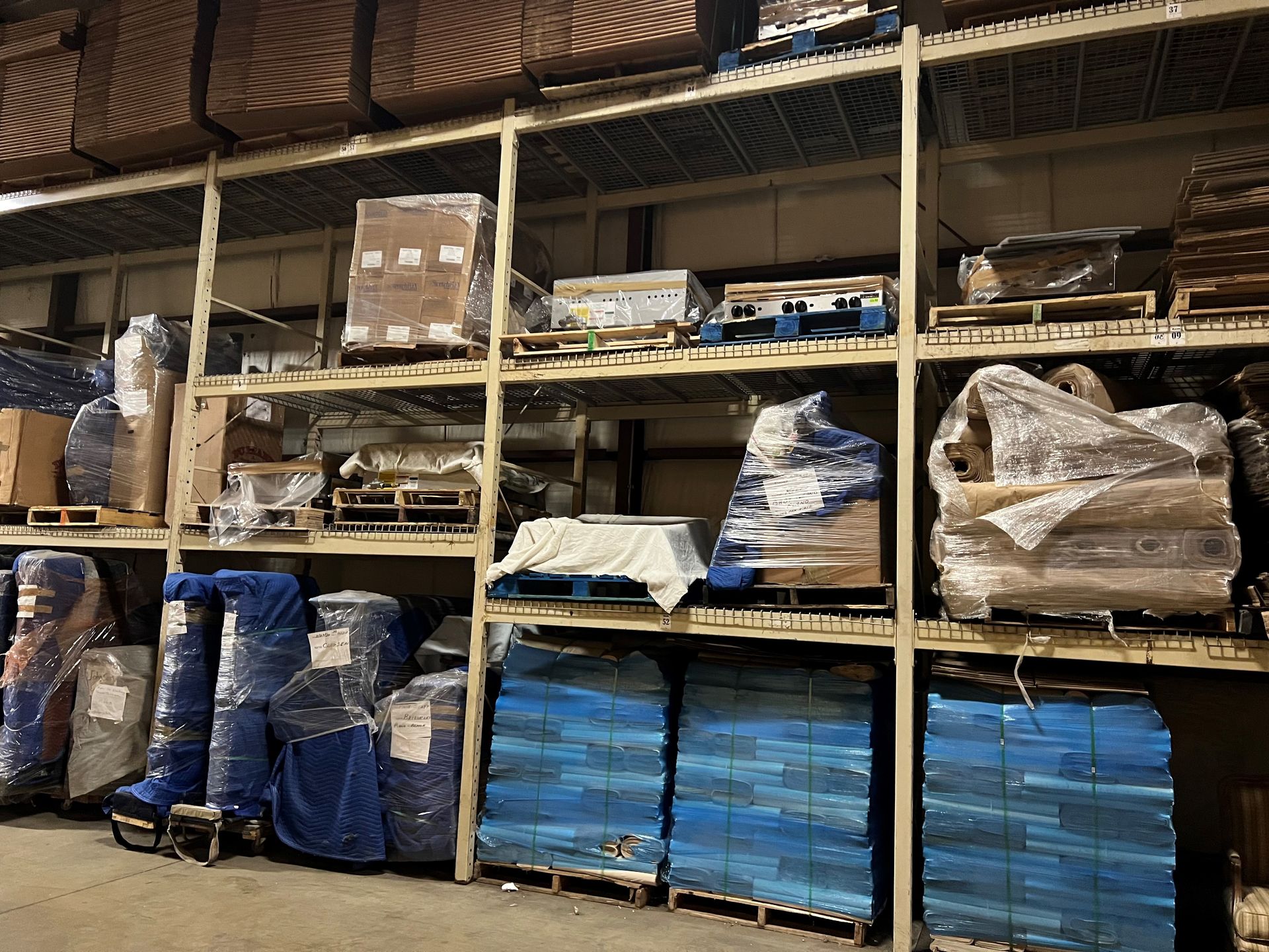 Warehouse shelving filled with packaged goods, including wood, blue pallets, and wrapped items.