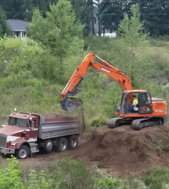 Excavator loading dirt into a dump truck on a hillside.