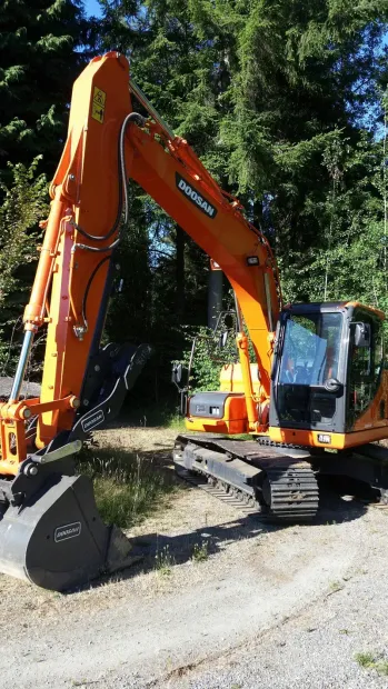 Orange Doosan excavator parked on gravel near trees.