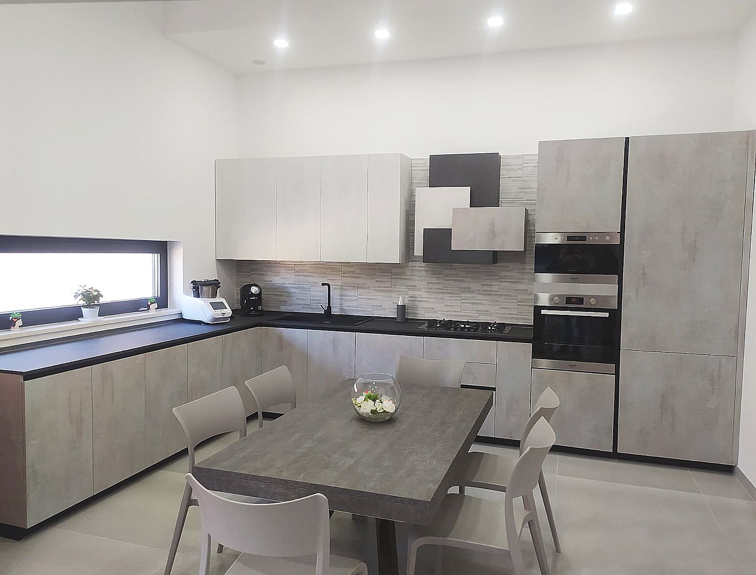 Moderna cucina grigia con mobili, elettrodomestici e tavolo da pranzo con sedie.