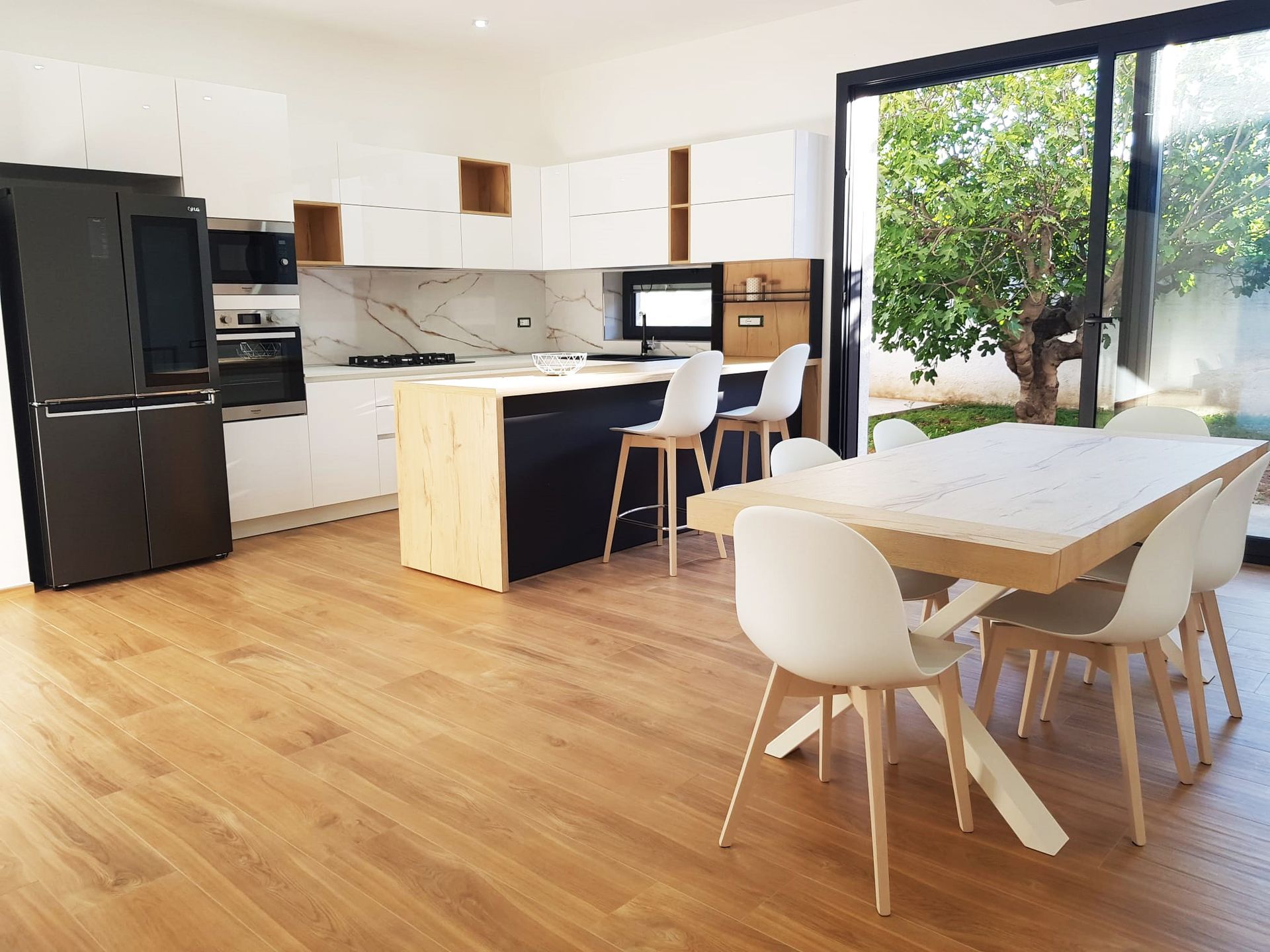 Cucina moderna con mobili bianchi, isola e tavolo da pranzo, con vista sul cortile.