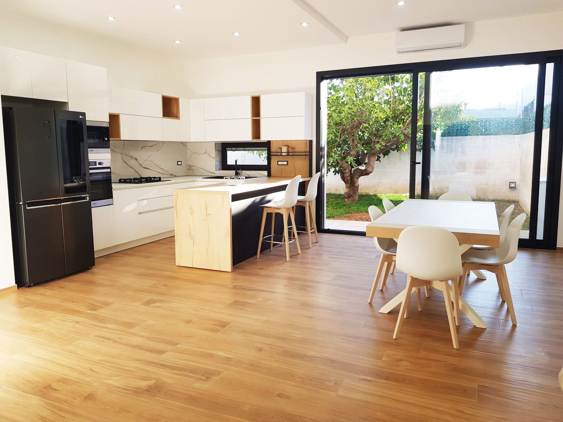 Cucina moderna con mobili bianchi e neri, isola in legno e zona pranzo con accesso all'esterno.