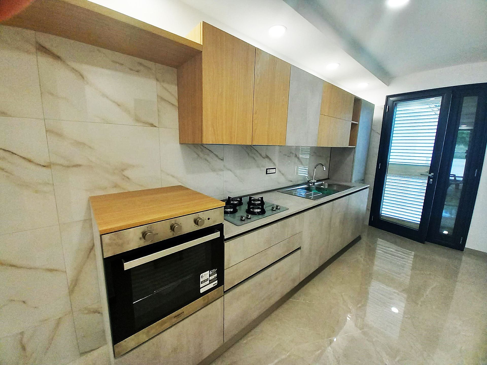 Cucina moderna con mobili in legno chiaro, paraschizzi in marmo, elettrodomestici in acciaio inox e porta in vetro.