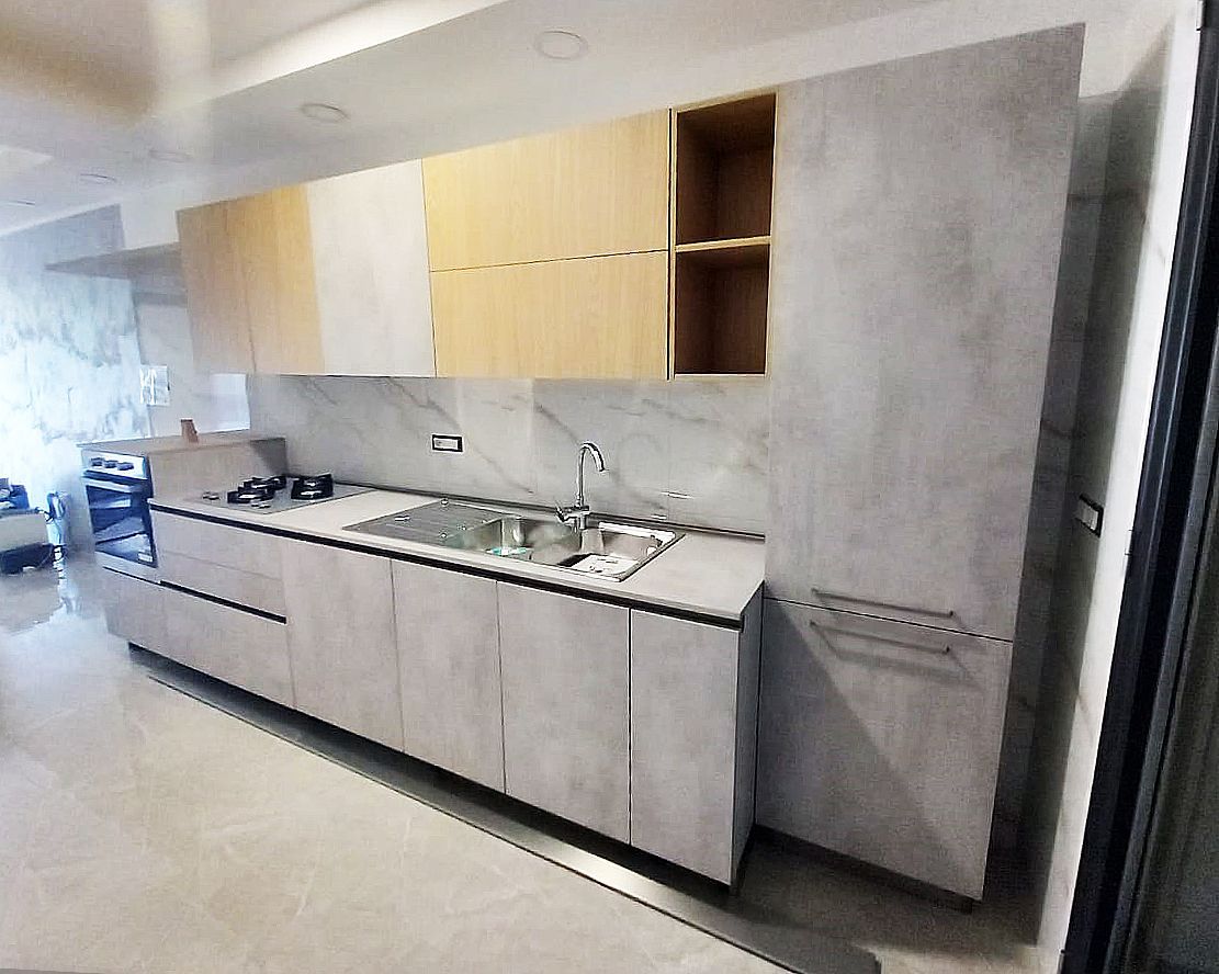 Cucina moderna con mobili grigio chiaro e legno, paraschizzi e ripiani in marmo, lavello ed elettrodomestici in acciaio inossidabile.