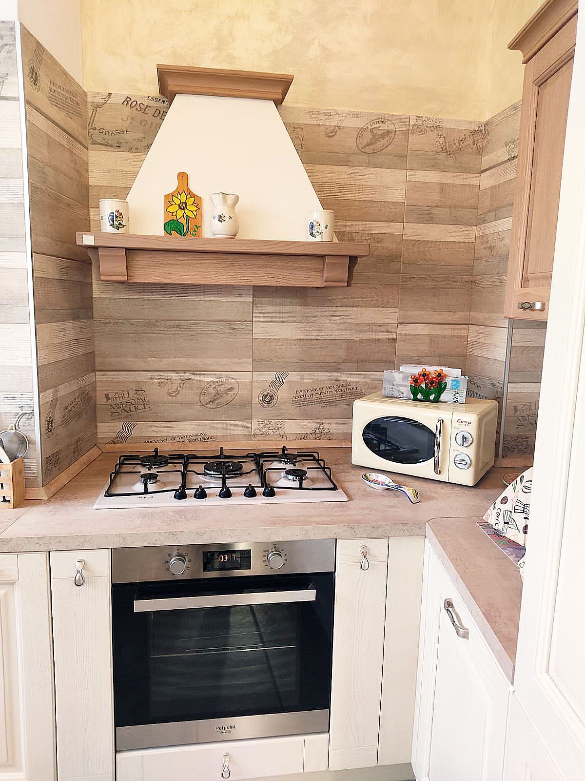 Cucina con piano cottura, forno, microonde e cappa aspirante. Tonalità beige e legno.