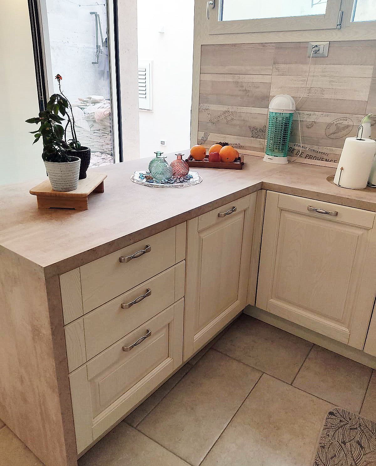 Mobili da cucina color crema con piano di lavoro in legno chiaro, cassetti e frutta, in uno spazio ben illuminato.