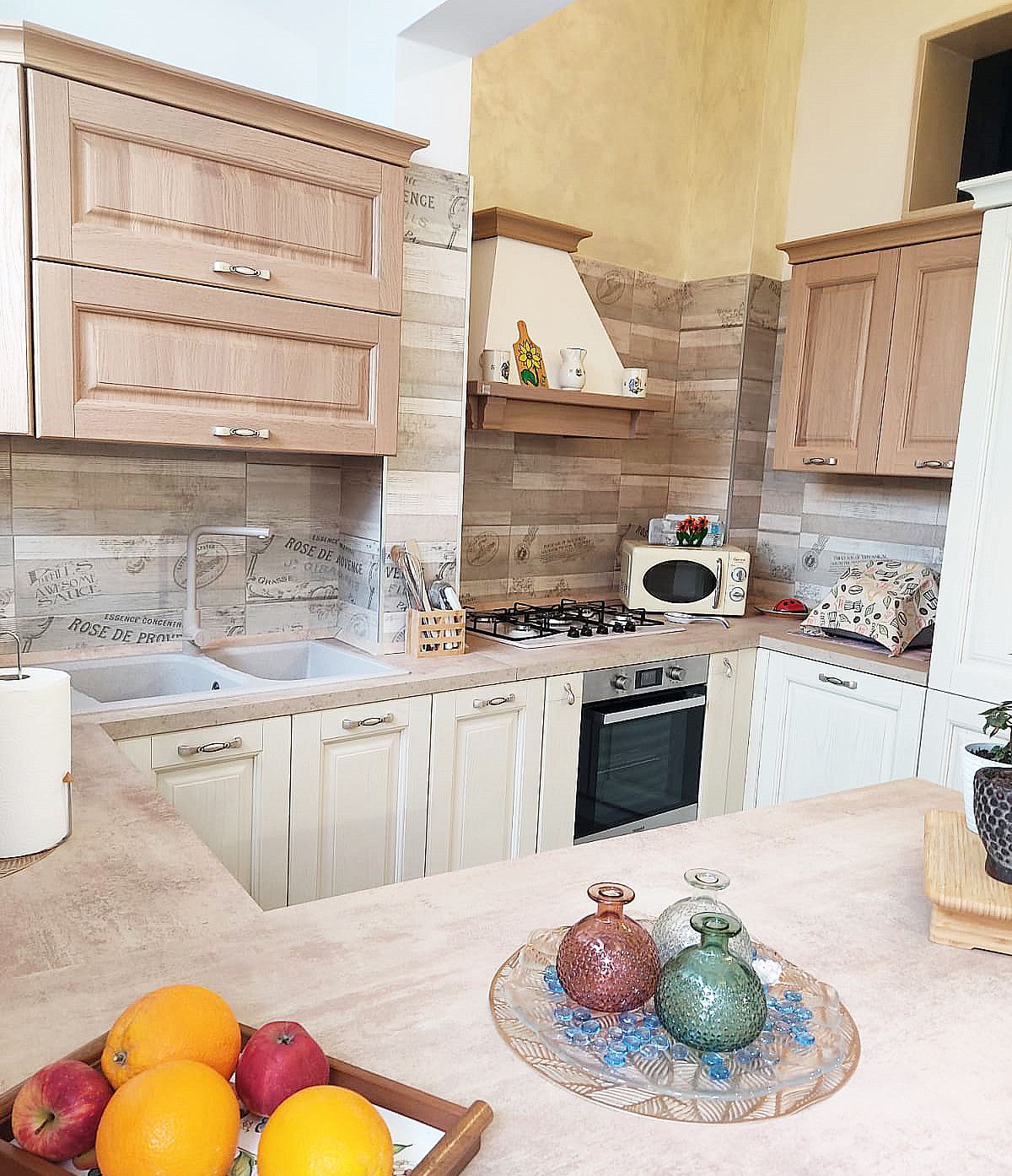 Cucina con mobili in legno, paraschizzi, fornelli e frutta sul piano di lavoro.