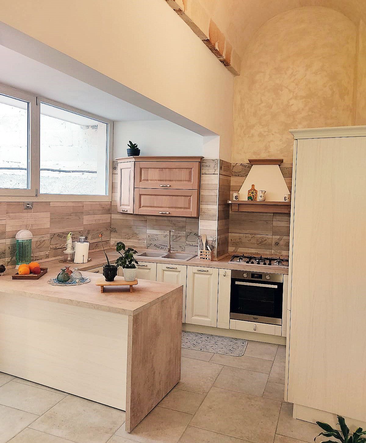 Cucina con paraschizzi in pietra, mobili bianchi e isola. La luce naturale inonda l'ambiente.