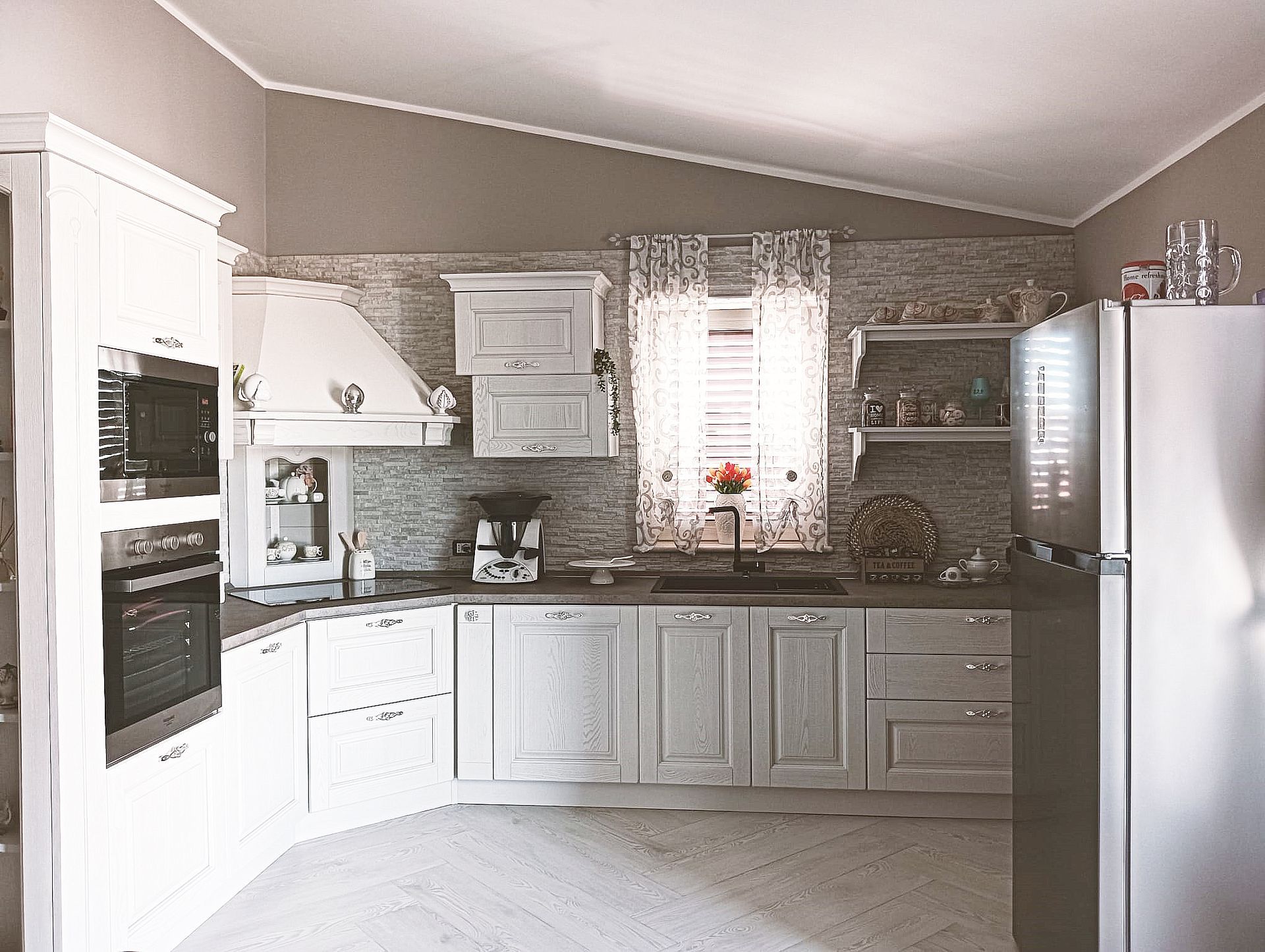 Cucina bianca con mobili, elettrodomestici e una finestra con tende.