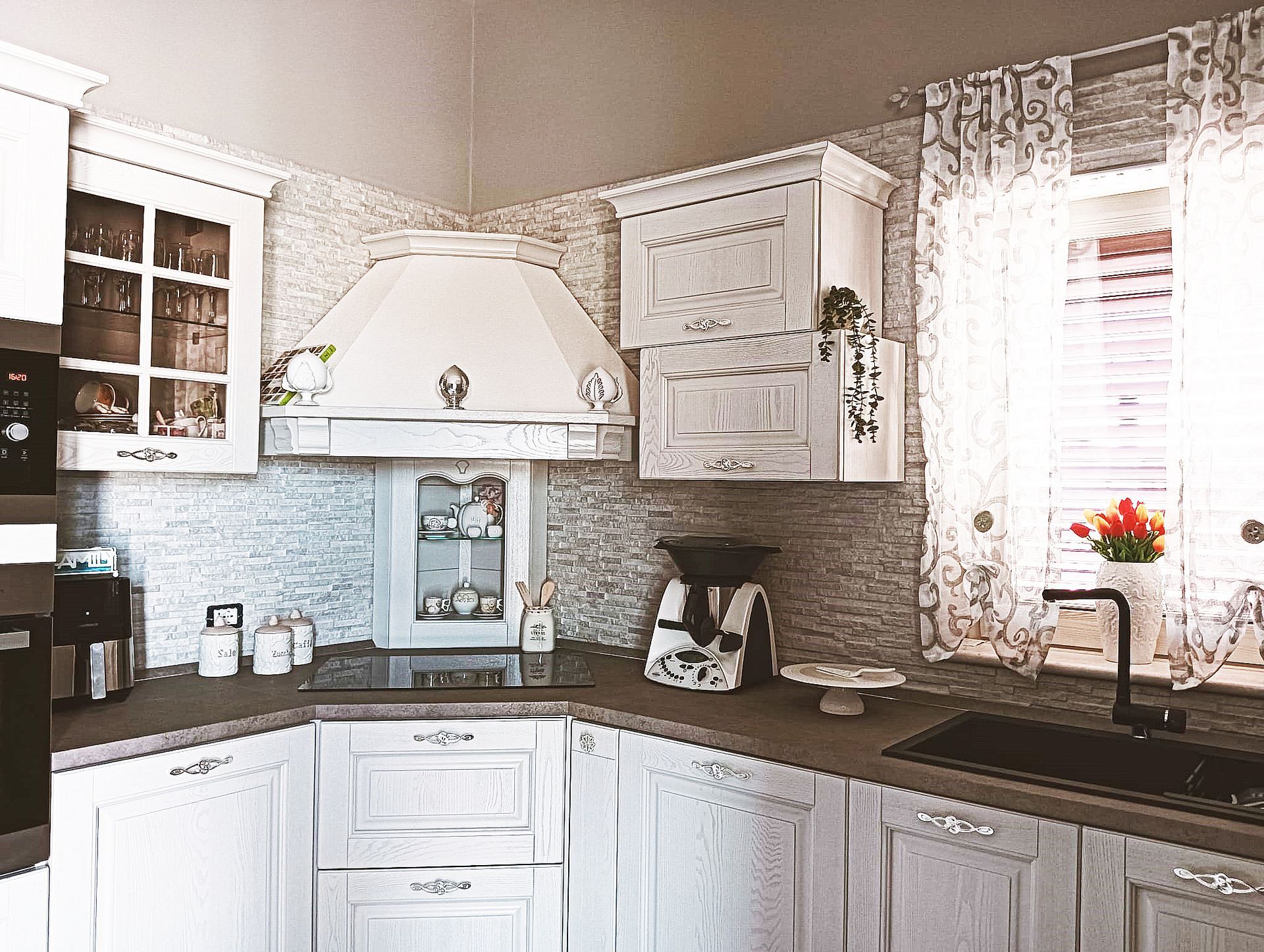 Cucina bianca con mobili decorativi, cappa aspirante e ripiani neri.