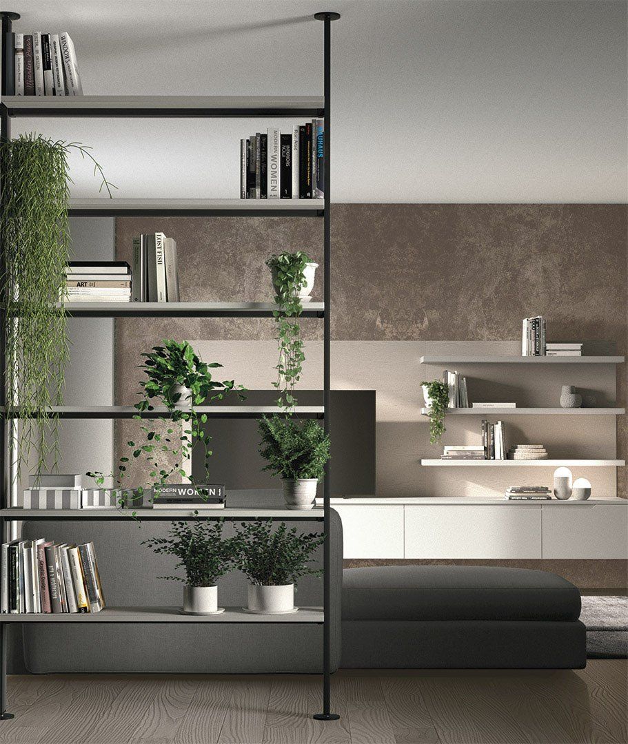 Scaffale moderno con libri e piante; un mobile bianco e un pouf scuro.
