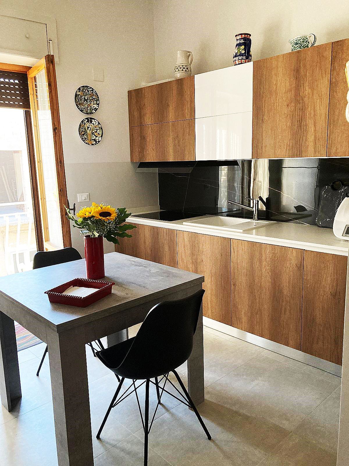 Cucina con mobili in legno, pensile bianco e tavolo da pranzo con sedie nere.