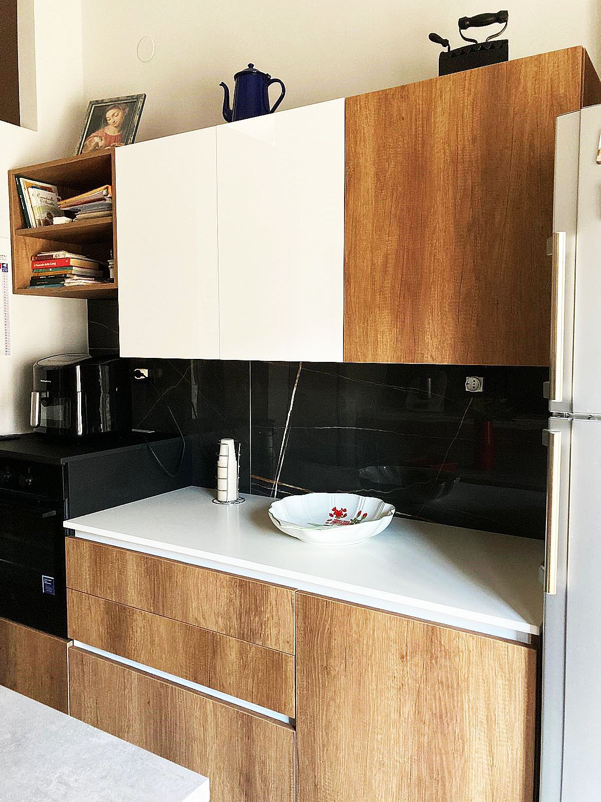 Cucina con mobili bianchi e in legno, paraschizzi nero, piano di lavoro bianco e vari elettrodomestici.